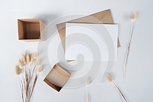Blank white paper on brown paper envelope with Rabbit tail dry flower and Carton box. Mock-up of horizontal blank greeting card.