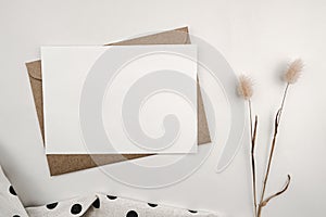 Blank white paper on brown paper envelope with Rabbit tail dry flower and White cloth with black dots. Mock-up of horizontal blank