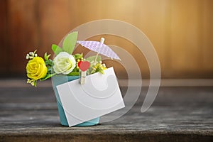 Blank white paper card on flower vas over blurred wooden background