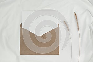 Blank white paper is placed on the open brown paper envelope with Bristly foxtail dry flower on white cloth. Mock-up of horizontal