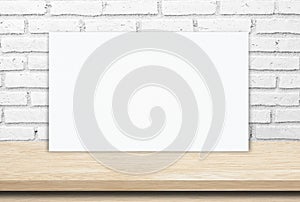 Blank white paper poster over wood table and brick wall background