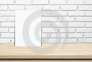 Blank white paper poster over wood table and brick wall background