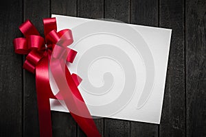 Blank white paper valentines or Christmas Greeting card with red ribbon on dark old wooden table background. picture for add text