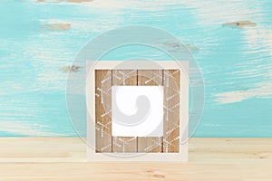 Blank white photo frame over wooden table and pastel blue background. Ready for photography montage