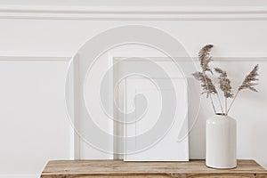 Blank white picture frame mockup. Vase with dry reed, grass on old wooden bench. Wall moulding background, trim decor