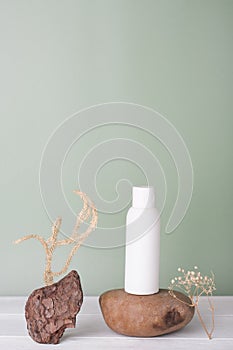 blank white plastic bottle, unbranded product. shampoo or sunscreen lotion. stone natural podium and dry plants decor