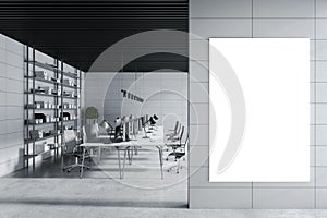 Blank white poster on grey wall in the foreground of modern industrial style co-working office with grey shades interior design,