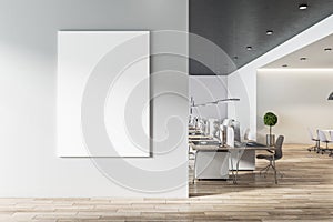 Blank white poster on light grey wall in modern open space office with light furniture and wooden floor. Mock up