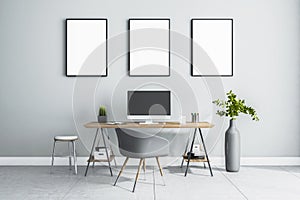 Blank white posters in black picture frame on light wall over stylish work place at home with monitor on wooden table, grey chair