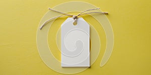 Blank white price tag tied with string on yellow background