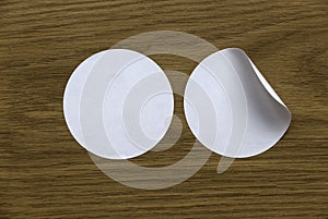 Blank white round stickers straightened and with folded corner on wooden background