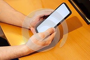 Blank white screen cell phone. Male hand texting using a mobile phone on a wooden table. Background empty space for advertising