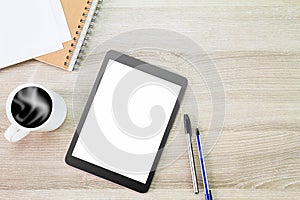 Blank white screen tablet computer with hot coffee cup, papers, notebook and pens on wooden desk