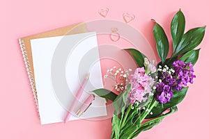 Blank white sheet on spiral golden notepad with paper clip heart and ring and bouquet of flowers on pink background. Concept