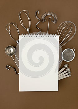 Blank white spiral notebook on metal kitchen utensils for pastries on brown table
