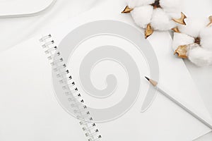 Blank white spiral notebook with pencil, cotton flowers and wooden letter on white bed sheet.