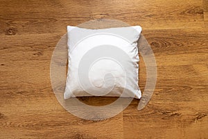 Blank white square pillow on a warm wooden floor background