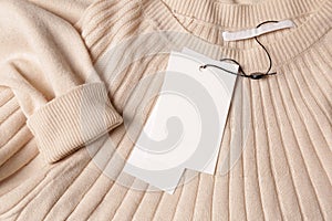 Blank white tags on beige sweater, top view. Space for text