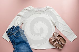 Blank white toddler girl`s long sleeved t-shirt on pink background with rose gold glitter ballet pumps and blue jeans