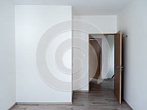 Blank white wall background in the empty room near the wooden opened door with copy space.