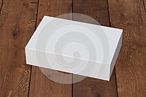 Blank white wide flat box with closed hinged flap lid on dark wooden background. Clipping path around box mock up.