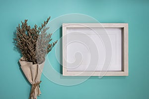 A blank white wooden frame with flower bouquet over the mint background.