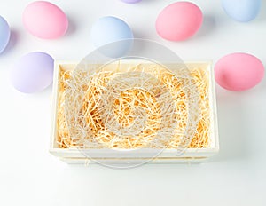 Blank wooden basket with wood wool on white background with pastel ester eggs
