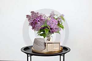 Blank wooden calendar next to bouquet of lilac flowers in vase and candlestick on an vintage coffee table, on an isolated white ba