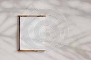 Blank wooden picture frame hanging on beige wall. Empty poster mockup for art display in sunlight. Minimal interior