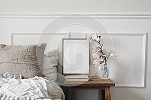 Blank wooden picture frame mockup on old book. Wooden night stand with fluted glass vase. Blooming magnolia tree