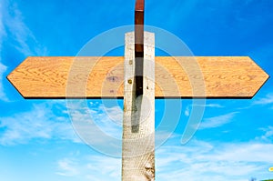 Blank wooden signpost with two arrows over clear blue sky with copy space