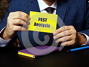 Blank yellow business card in a hand with phrase Sociological, Technological, Economical and Political Change PEST Analysis .