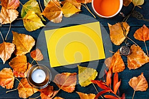 A blank yellow greeting card or invitation with a cup of a tea, autumn leaves and a candle, an autumn stationery mockup