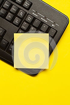 Blank yellow paper note on a black computer keyboard on a yellow background