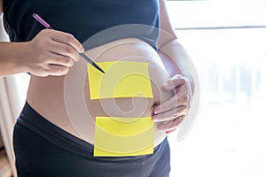 Blank yellow sticker notes on the pregnant woman`s belly. FAQ concept.