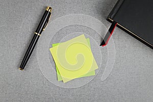 Blank yellow sticky note with black and gold fountain pen and black cover book with red and black bookmark.