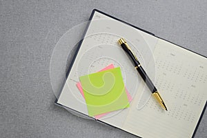Blank yellow sticky note and black and gold fountain pen placed on calendar notebook.