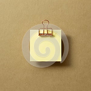 Blank yellow sticky note pad and metal clip on brown background