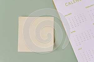 Blank yellow sticky note with yearly calendar on green background