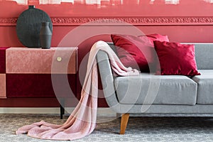 Blanket and burgundy pillows on grey sofa in trendy living room interior with chest of drawers