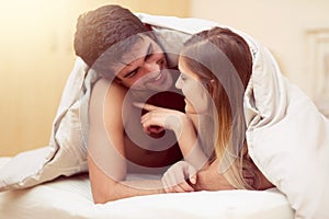 Blanket, conversation and couple in bed for love with intimacy together, happy relationship and talking for trust photo