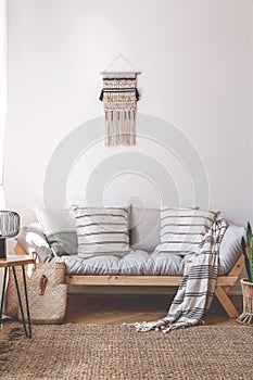 Blanket and cushions on wooden couch in beige living room interior with brown carpet. Real photo photo