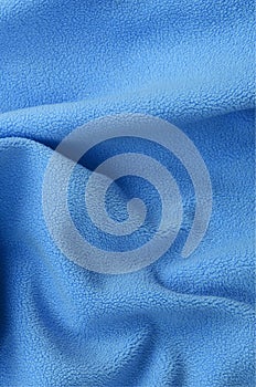 The blanket of furry blue fleece fabric. A background of light blue soft plush fleece material with a lot of relief folds