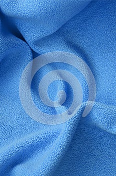 The blanket of furry blue fleece fabric. A background of light blue soft plush fleece material with a lot of relief folds