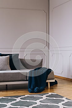 Blanket and pillows on grey comfortable sofa in designed living room interior with wooden floor and white wall