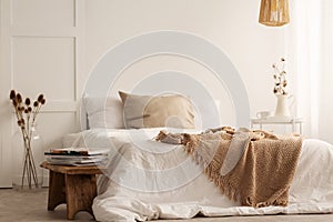 Blanket on white bed in natural bedroom interior with plants and wooden stool photo