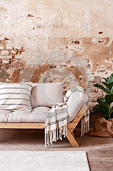 Blanket on wooden beige couch against red brick wall