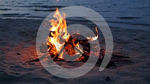 Blazing campfire on beach, summer evening. Bonfire in nature as background. Burning wood on white sand shore at sunset.