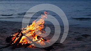 Blazing campfire on beach, summer evening. Bonfire in nature as background. Burning wood on white sand shore at sunset.