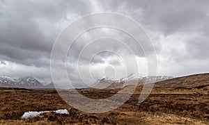 A bleak and wet Rannoch Moor near to Loch Ba, on a wet day in April, with surrounding snow topped Mountains.